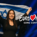 Израильская участница поднимает флаг Израиля на сцене Eurovision Song Contest на фоне ярких синих прожекторов и логотипа конкурса.
