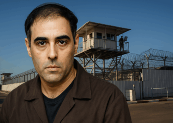 Игаль Амир на фоне тюремной охранной башни и высокого забора с колючей проволокой.